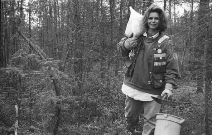 Young woman in a dense forest carrying a bucket of soil and bag over one shoulder. 