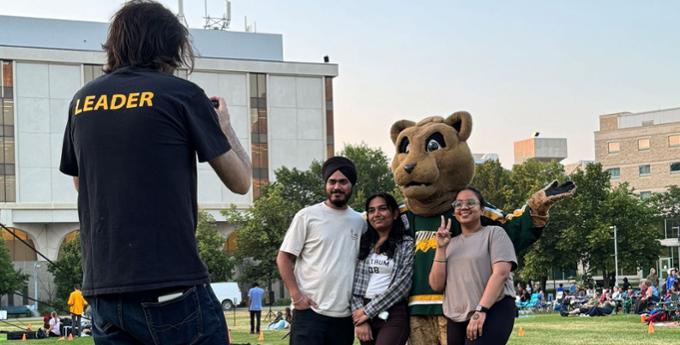 3 people posing with the U of R mascot and another taking a photo