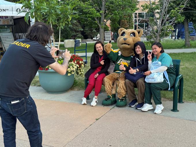 3 people posing with the U of R mascot and another taking a photo