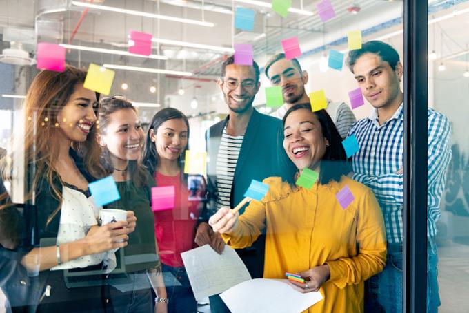 Team collaborating at a clear board with Post-It notes. 