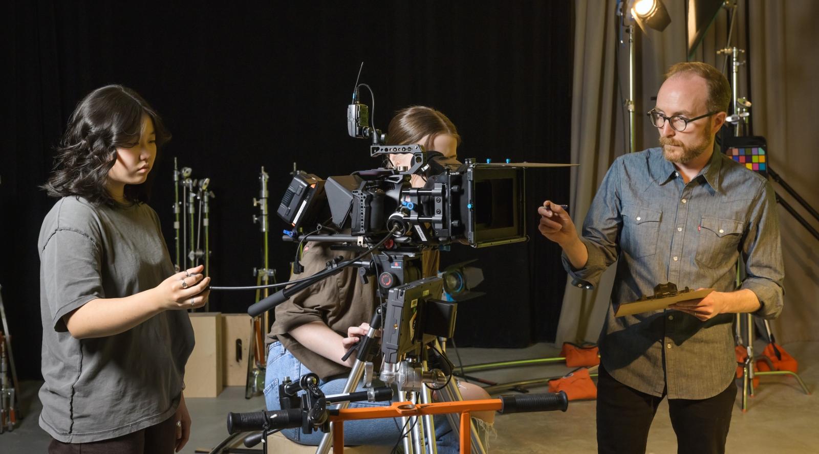 Two students and a professor working with a camera