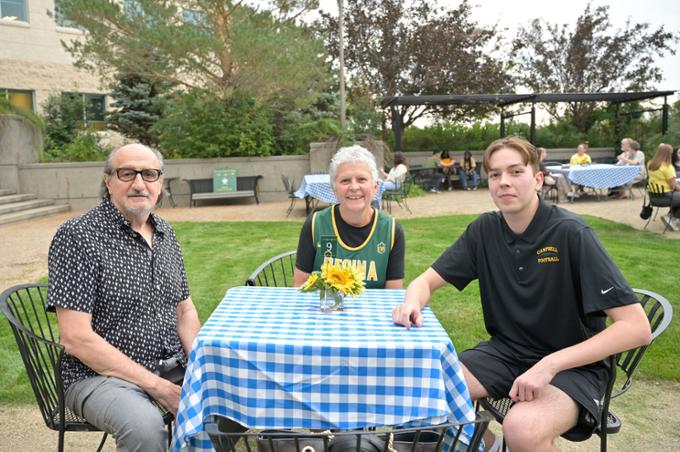 Three people sit at table with blue checkered tablecloth.