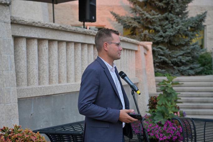 Man outdoors speaking at microphone at twilight..