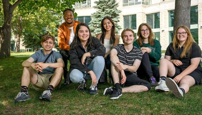 UofR students seated outdoors on the grass looking at the camera smiling