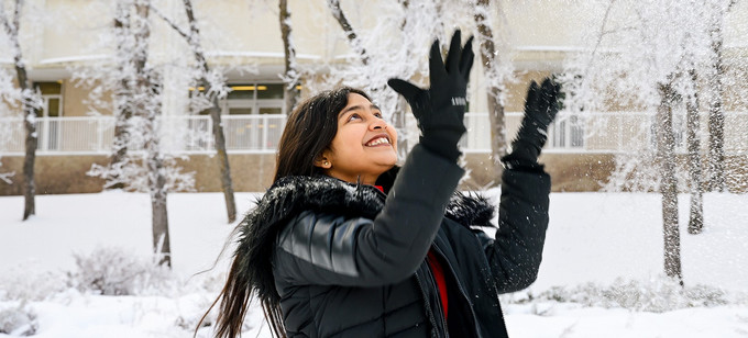 Student stands outside throwing snow into sky.