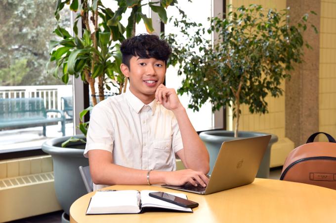 Student at table with laptop smiling at camera.