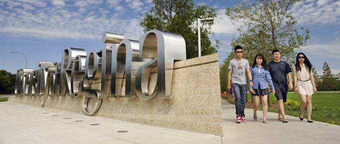 A group of four students walk on a path beside the University of Regina sign