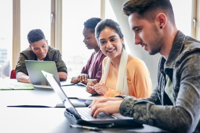 A group of students learning together with laptops open on desks.