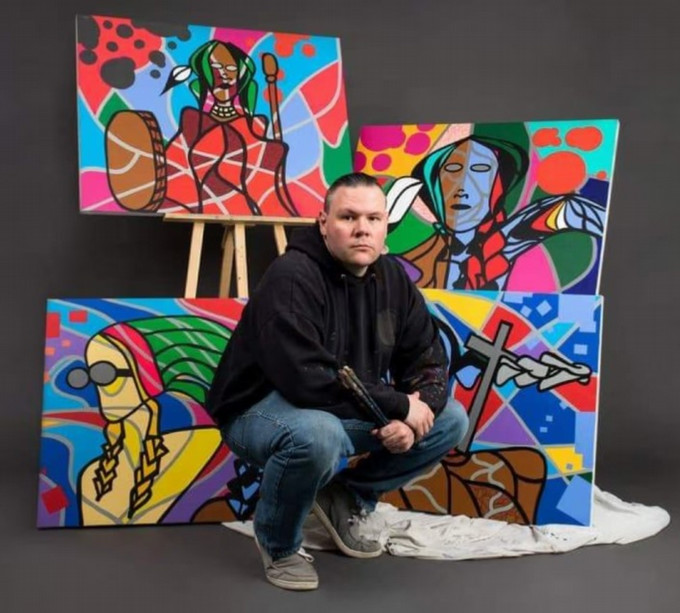 a man crouching in front of four colourful paintings