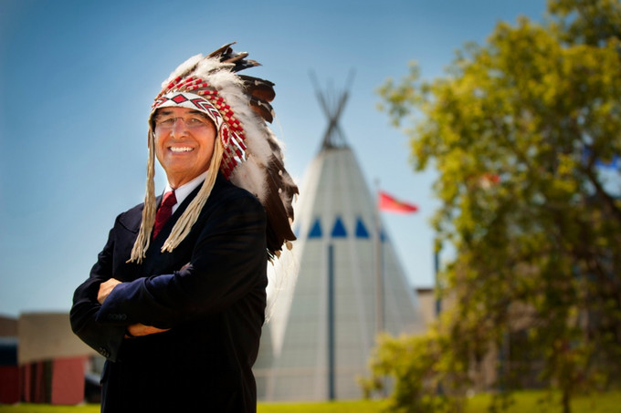 a man standing infront of a tipi, wearing traditional headdress