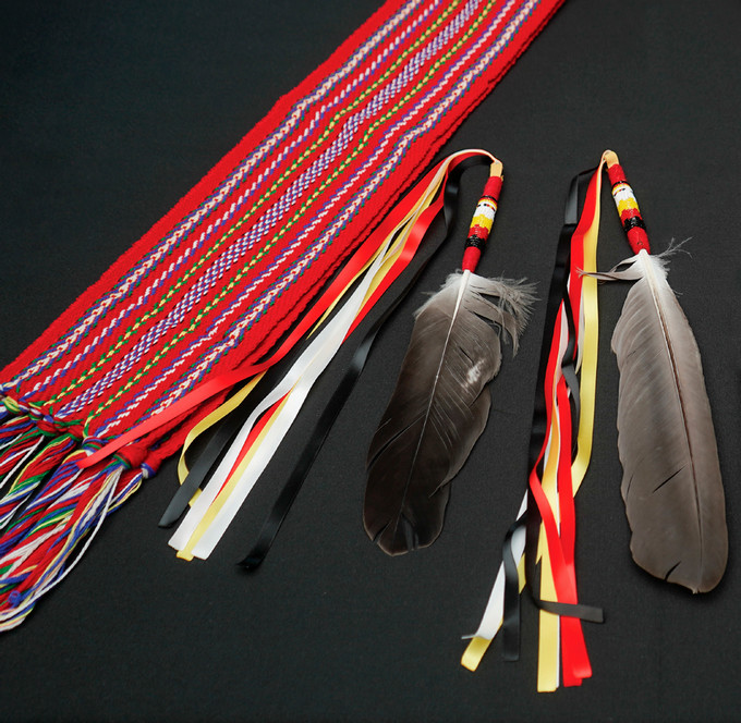 photograph of metis sash and eagle feather on black background