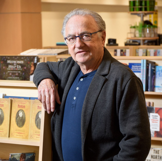 author in a bookstore, leaning against a shelf displaying his books