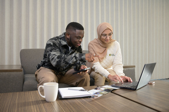 Two students sitting on a couch doing schoolwork on a laptop