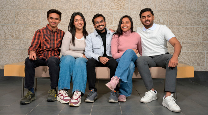 Five students sitting on a bench and smiling at the camera