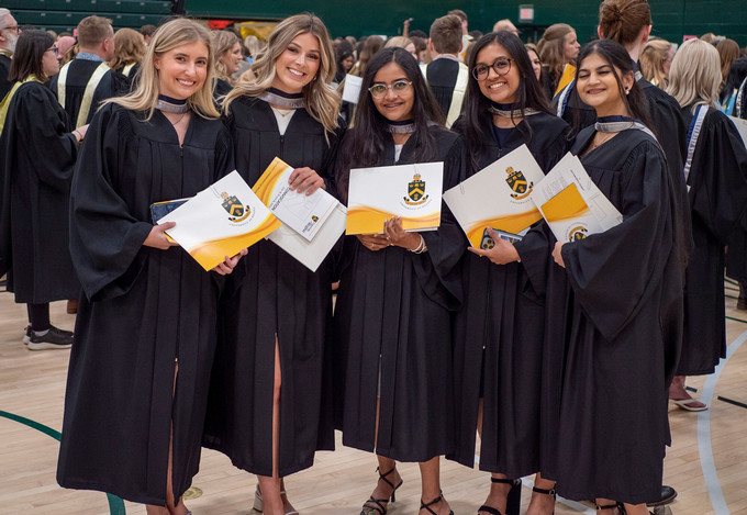 Five graduating students posing for the camera, holding their degree folders