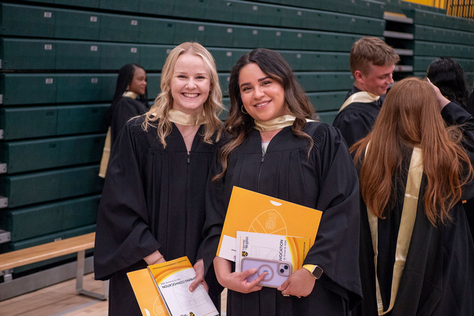 two students in their convocation gowns with their diplomas