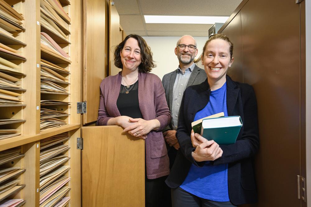 Three people stand amongst archival material