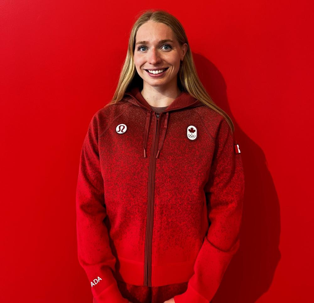 A young woman is photographed in a Canadian Olympic top against a red background. 