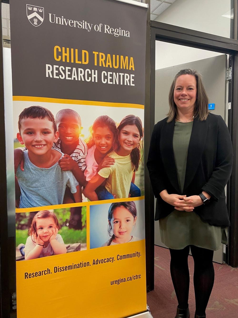 Woman standing to right of a full-length sign with faces of children on it.