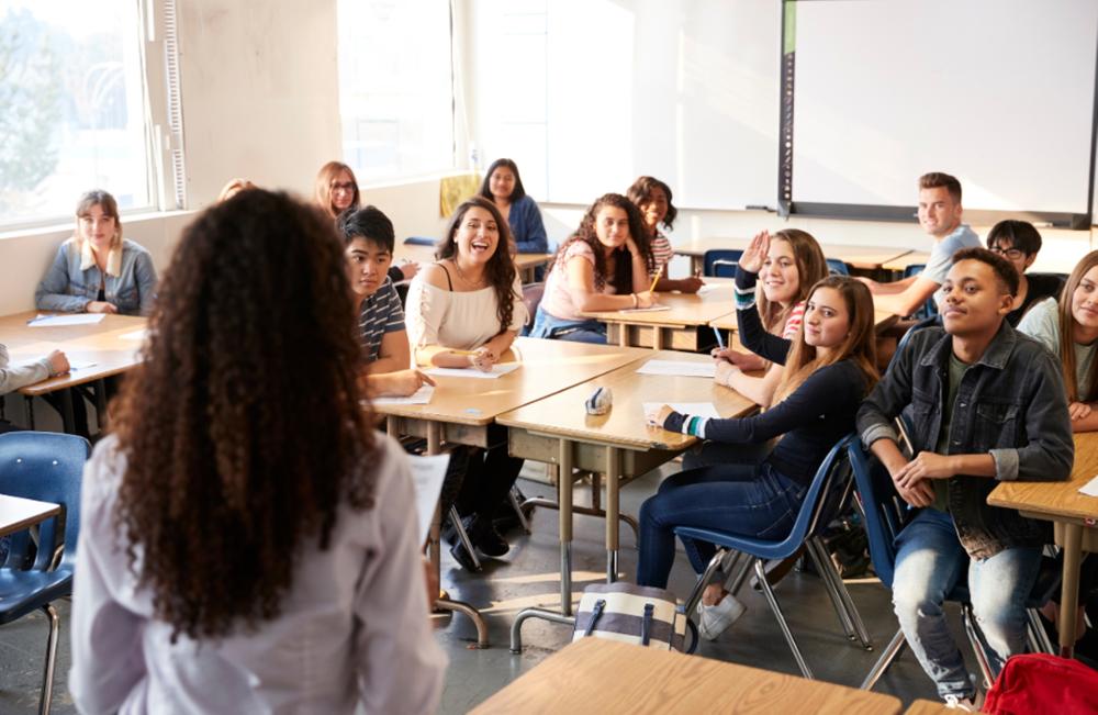 Young people sitting at desks in a classroom with whiteboards in the background.