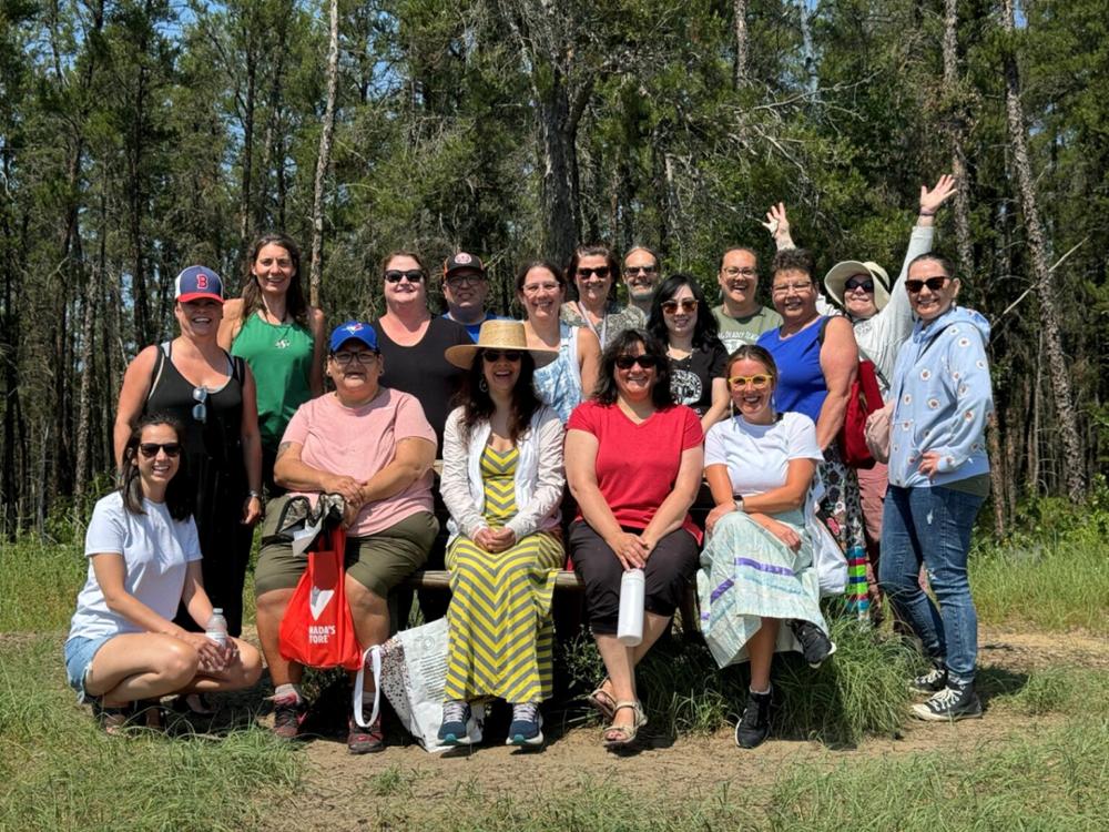 A group of students standing outside in front of tall green trees.