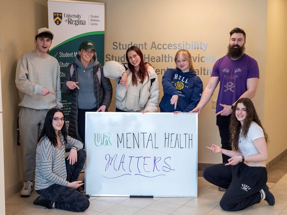 A group of students surround a sign that says “UR Mental Health Matters.”