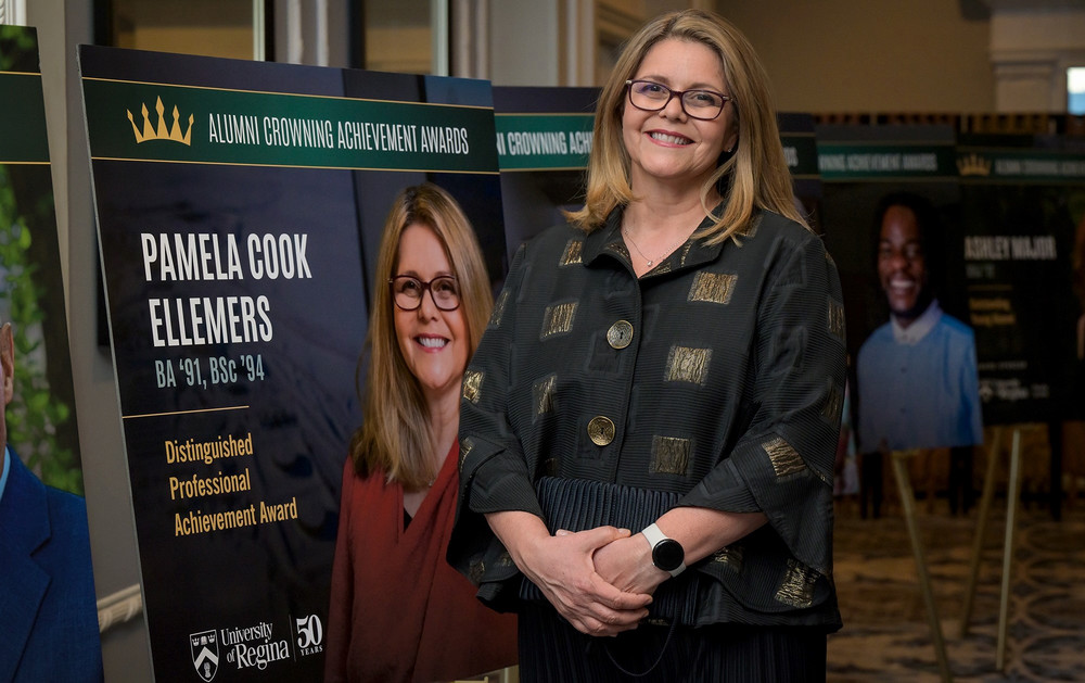 Woman wearing glasses standing in front of a poster board with her photo and the name of the award she received.