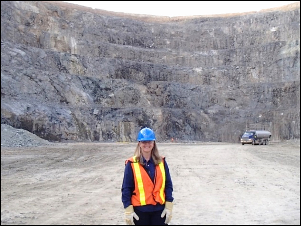 Woman with hard hat standing in an open mining pit.