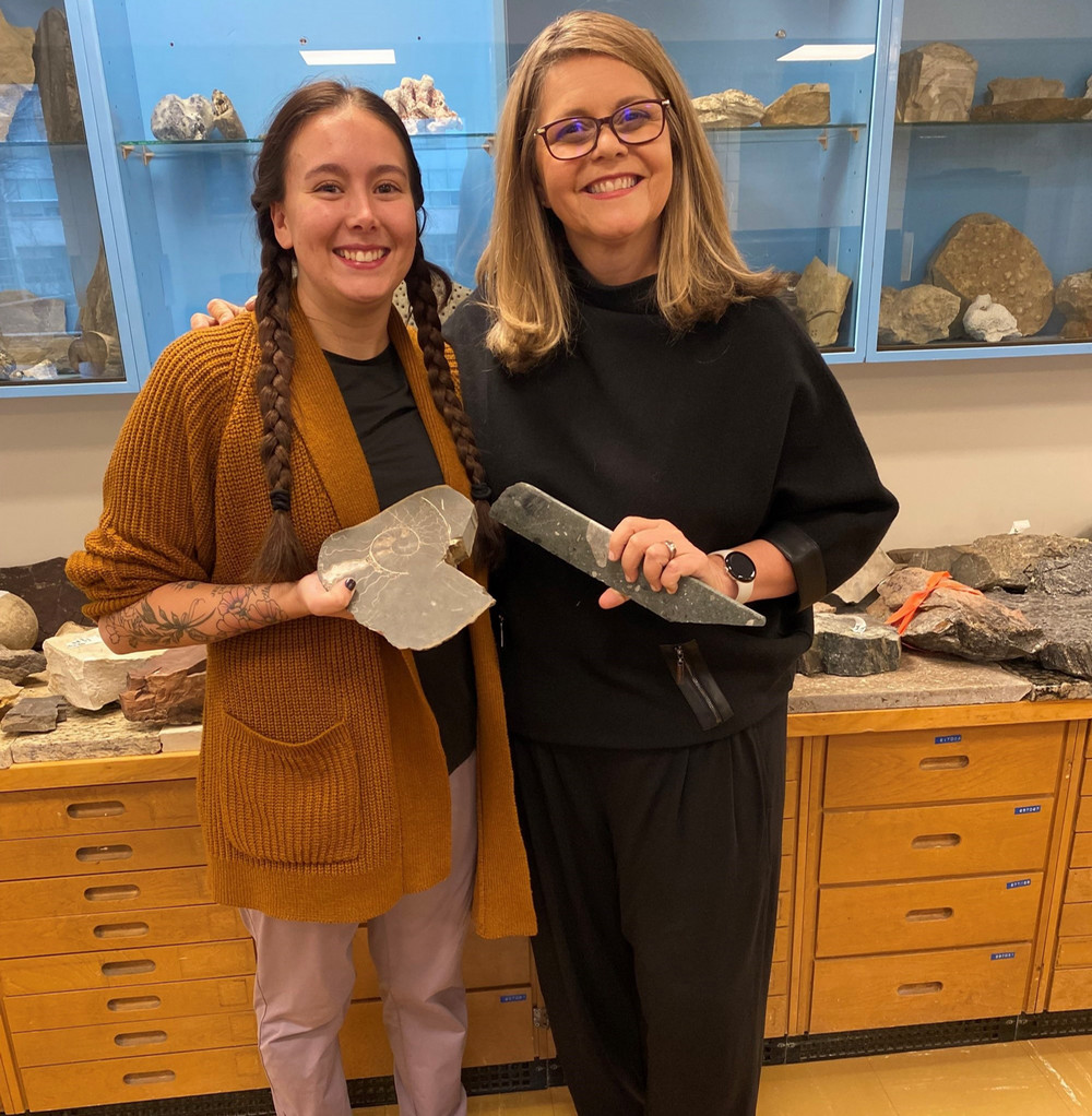 Two women smiling and standing holding rocks in a lab.