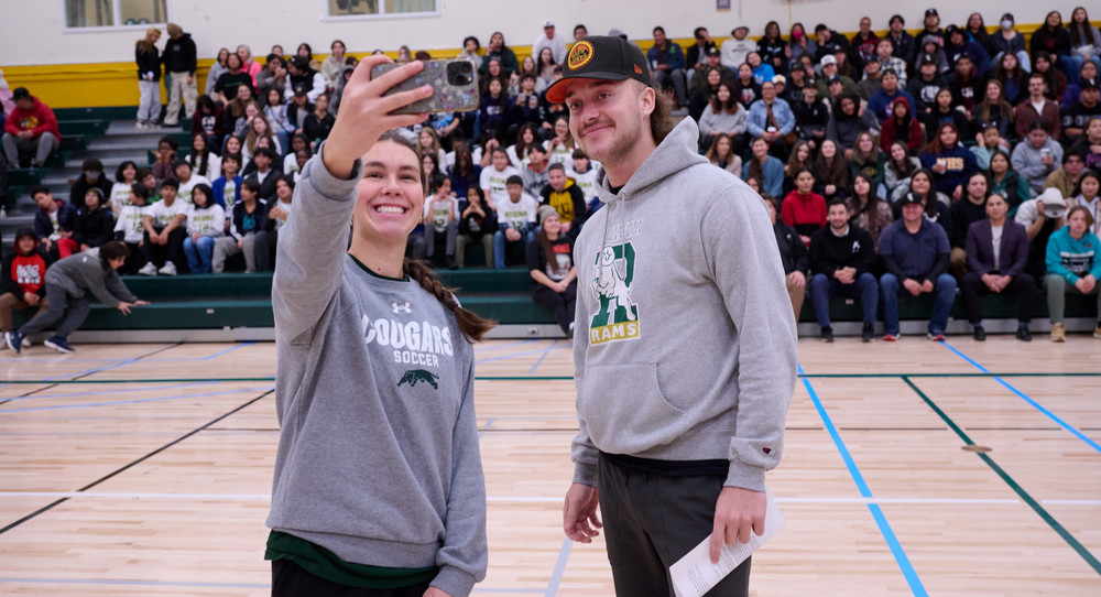 Two student athletes taking a photo of themselves with a group of high school students.