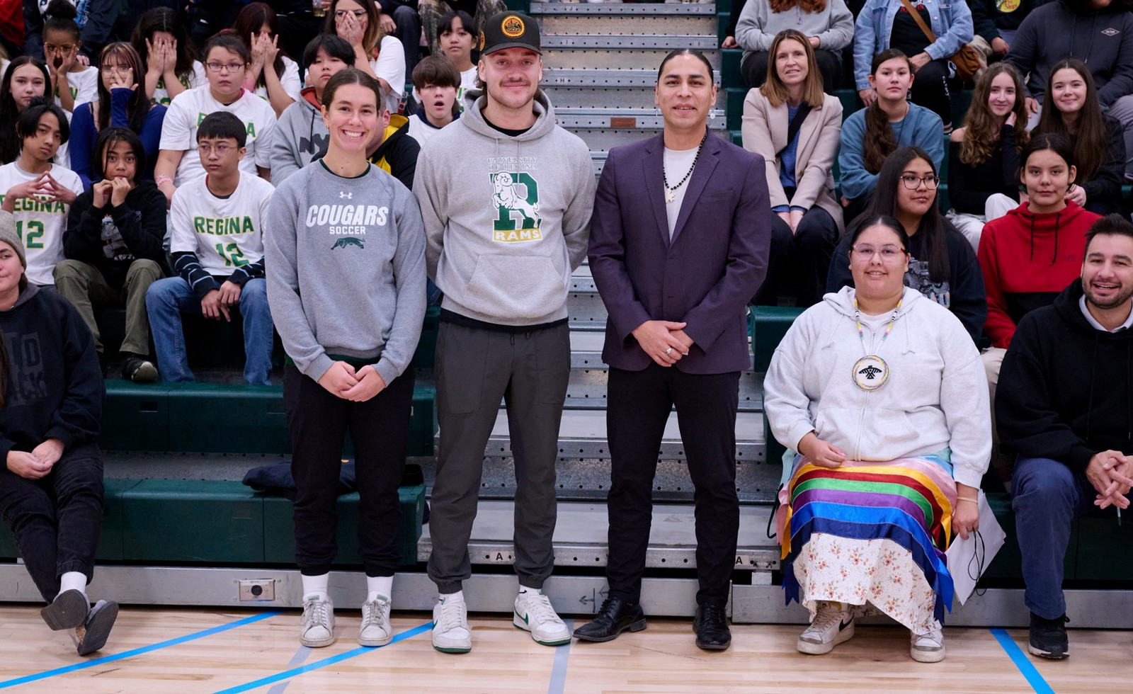 A group of individuals sitting on bleachers in a university gym.