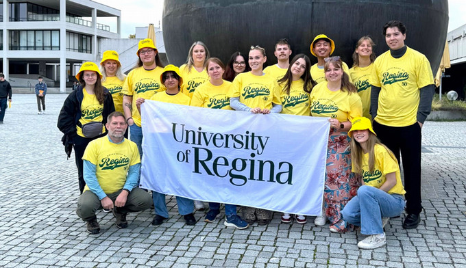 A group of individuals wearing University of Regina t-shirts and holding a University of Regina sign.