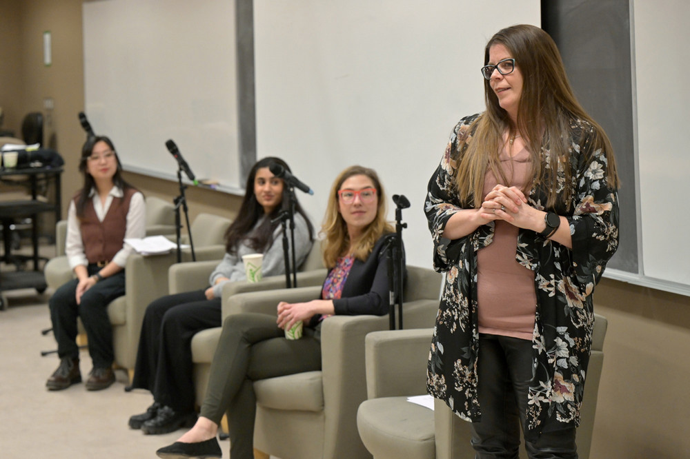 Four individuals, three sitting and one standing, speaking at a panel discussion event.