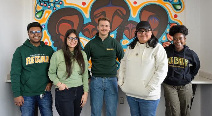 Five students standing infront of a mural.