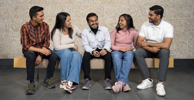 Five students sitting on bench laughing.