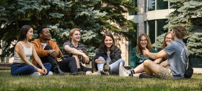 Students sitting on lawn talking and smiling.