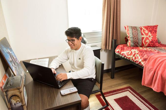 Student sitting at desk in housing room. 