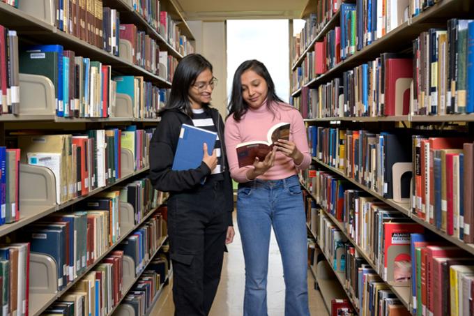 Two students looking at a book in the library.