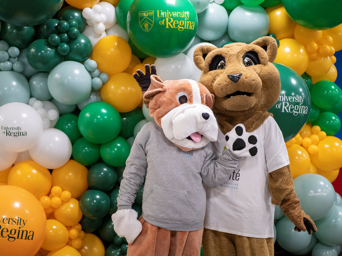 Two mascots pose in front of a wall of colourful balloons